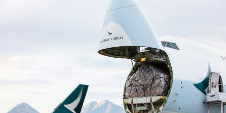 A Cathay Cargo airplane with its nose open against a backdrop of mountains