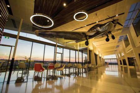 Tables at bay windows in airport, with sculpture of propeller aircraft hanging overhead