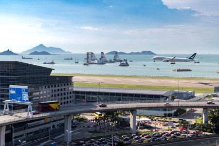 Cathay aircraft landing at HKIA with terminal, taxi rank, flyover, and sea visible