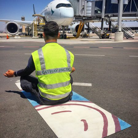Ground crew in meditative seated posture on yoga mat in front of Cathay aircraft