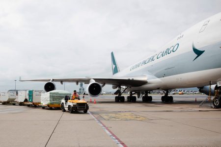 A Cathay aircraft on the tarmac with a cargo tractor approaching