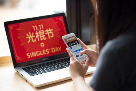 Woman using ecommerce platform on smartphone, and full screen singles' day poster on laptop