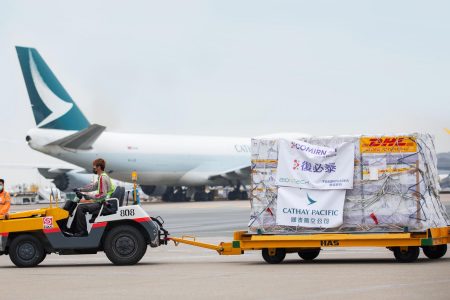 Baggage tractor carrying comirnaty vaccine shipment in front of aircraft