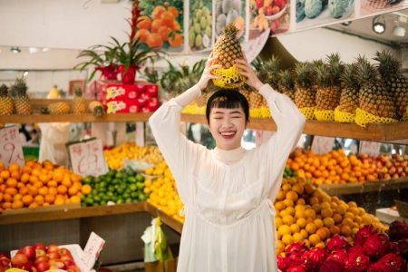 Lady in fruit market holding a pineapple over her head