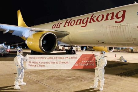 Team members wearing full PPE holding banner in front of air HongKong aircraft