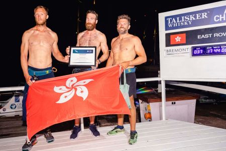 The three members of the East Rows West rowing team posing for a photo onstage, holding the Hong Kong SAR flag and an achievement certificate