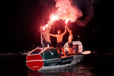 East rows west team members celebrate holding flares in boat at night