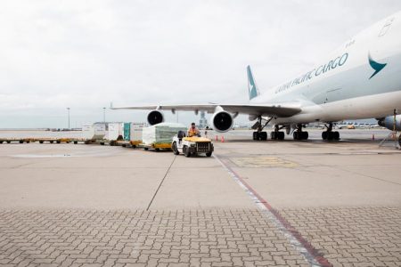 Baggage tractor with cargo near Cathay aircraft on tarmac
