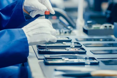Close up of factory worker with gloved hands assembling smartphone components 