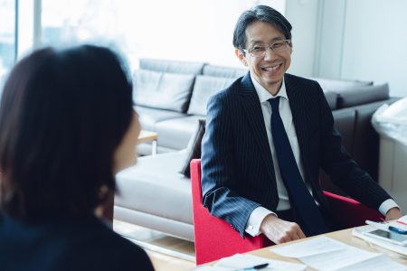 Shuichi Ueba smiling at desk in office with colleague