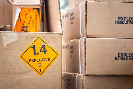 Stacked boxes with explosive warning labels including '1.4 EXPLOSIVE' and 'CARGO AIRCRAFT ONLY.