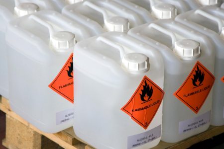 White plastic jerry cans labeled 'FLAMMABLE LIQUID' and 'ALCOHOLS, N.O.S. (PROPAN-1-OL, ETHANOL)' arranged on a wooden pallet, indicating hazardous chemical storage.