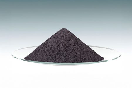 Conical pile of dark gray powder on a glass dish, displayed against a gradient teal-to-gray background, representing particulate material.