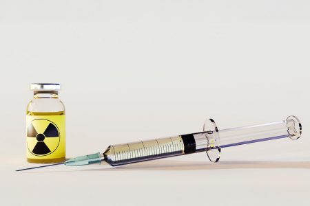 Syringe and vial filled with yellow liquid, with the vial labeled with a radiation hazard symbol, indicating radioactive material handling.