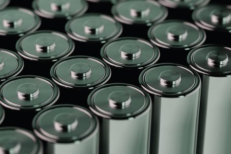 Close-up image of lithium-ion cylindrical batteries with metallic tops and central terminals, arranged in rows for energy storage or transport.